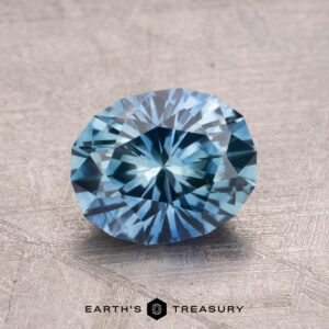 A faceted blue gemstone, the 1.66-Carat Montana Sapphire (Heated), is displayed on a textured surface, with the text "Earth's Treasury" at the bottom.