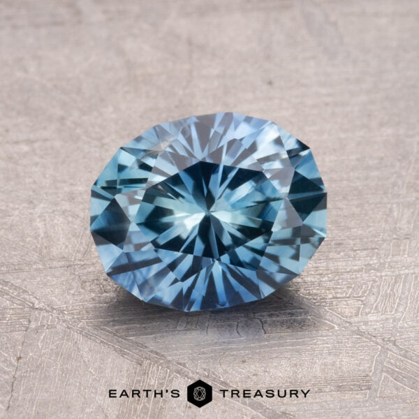 1.66-Carat Montana Sapphire (Heated) A faceted blue gemstone, the 1.66-Carat Montana Sapphire (Heated), is displayed on a textured surface, with the text "Earth's Treasury" at the bottom.