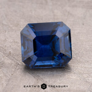 A faceted 2.24-carat Ceylon Sapphire, possessing a striking light violet-blue hue and rectangular shape, is elegantly placed on a textured surface. The words "Earth's Treasury" are gracefully displayed beneath it.