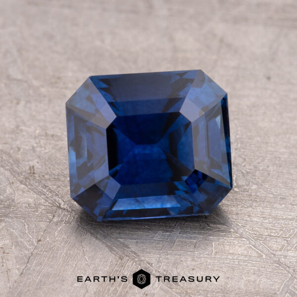 2.24-Carat Ceylon Sapphire (Heated) A faceted 2.24-carat Ceylon Sapphire, possessing a striking light violet-blue hue and rectangular shape, is elegantly placed on a textured surface. The words "Earth's Treasury" are gracefully displayed beneath it.