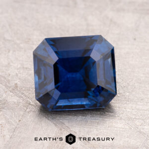 A faceted 2.24-carat Ceylon Sapphire, possessing a striking light violet-blue hue and rectangular shape, is elegantly placed on a textured surface. The words "Earth's Treasury" are gracefully displayed beneath it.