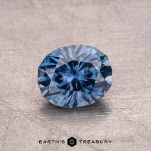 A faceted 1.18-carat Montana sapphire (heated) displayed on a textured surface.