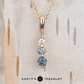 The "Dawn" Necklace in 14k yellow gold features a pendant with three vertically arranged round stones—one white and two blue. The image displays the "Earth's Treasury" logo at the bottom.