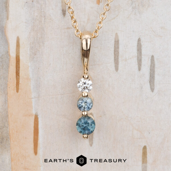 The "Dawn" Necklace in 14k yellow gold The "Dawn" Necklace in 14k yellow gold features a pendant with three vertically arranged round stones—one white and two blue. The image displays the "Earth's Treasury" logo at the bottom.