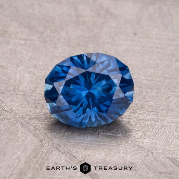 1.11-Carat Montana Sapphire (Heated) A 1.11-carat Montana Sapphire with a deep blue hue and intricate facets rests on a textured surface.
