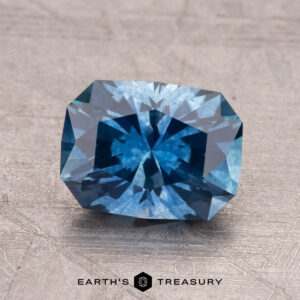 A 2.01-carat rectangular cut sapphire with a blue hue is shown on a textured surface, with the "Earth's Treasury" logo at the bottom.