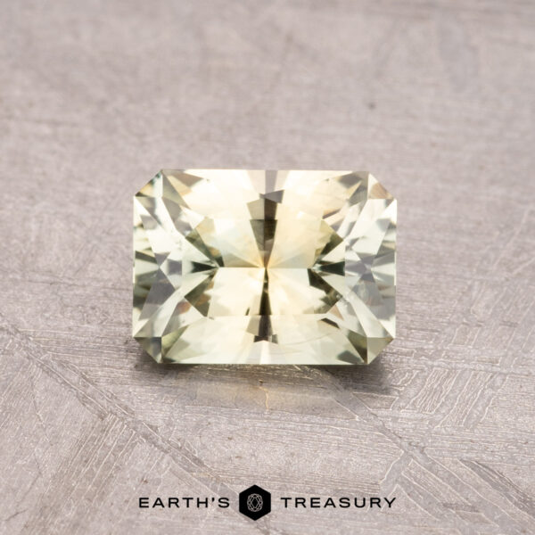 1.12-Carat Montana Sapphire (Heated) A 1.12-carat Montana sapphire in a faceted yellow-green hue is showcased on a textured surface, accompanied by the "Earth's Treasury" brand logo below.