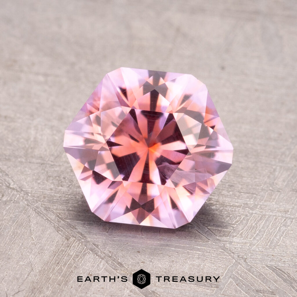 A 1.89-carat Montana Sapphire, expertly cut into a faceted hexagonal shape with intricate detailing, is showcased on a textured surface, accompanied by the Earth’s Treasury logo at the bottom.