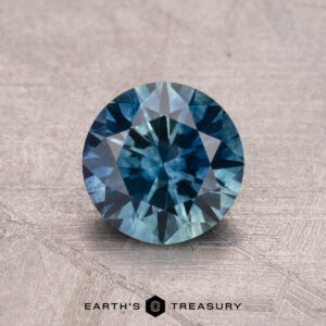 A round blue 1.19-carat Montana sapphire, known for its intricate facets, is displayed on a textured surface, with the "Earth's Treasury" text and logo below.