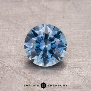 1.04-carat Montana sapphire with a brilliant cut on a textured surface, branded "Earth's Treasury.