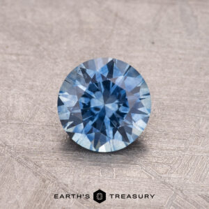 0.81-carat Montana sapphire, heated, featuring a brilliant blue gemstone with glistening facets on a textured gray surface.