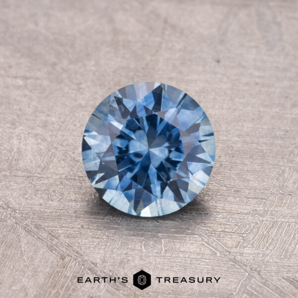 0.81-carat Montana sapphire, heated, featuring a brilliant blue gemstone with glistening facets on a textured gray surface.