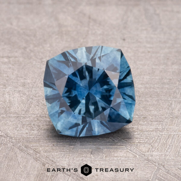 1.27-Carat Montana Sapphire (Heated) A faceted cushion-cut blue 1.27-carat Montana Sapphire (heated) on a textured surface with the text "Earth's Treasury" below.