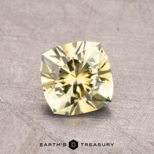 A 0.99-carat heated Montana Sapphire in a faceted cut, displayed on a textured gray surface with the text "Earth's Treasury" at the bottom.