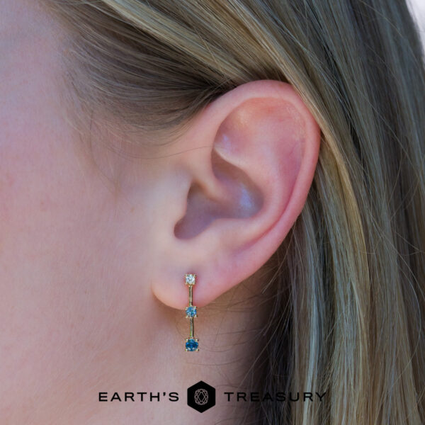 dusk earring Close-up of a person's ear wearing the elegant dusk earring with two colored stones set in gold. The "EARTH'S TREASURY" logo appears at the bottom of the image.