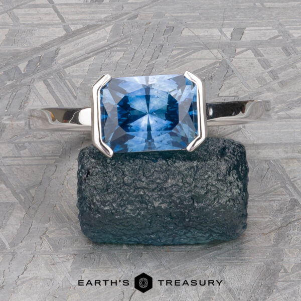 The "Lina" ring in 14k white gold with 2.34-Carat Montana Sapphire A "Lina" ring in 14k white gold with a 2.34-carat Montana sapphire is displayed on a textured blue stone, with "EARTH'S TREASURY" text below.