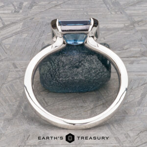 The "Lina" ring in 14k white gold, featuring a 2.34-carat Montana Sapphire, is displayed upright on a blue textured stone with the Earth's Treasury logo at the bottom.