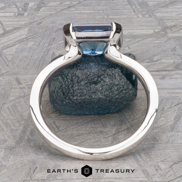 The "Lina" ring in 14k white gold with 2.34-Carat Montana Sapphire The "Lina" ring in 14k white gold, featuring a 2.34-carat Montana Sapphire, is displayed upright on a blue textured stone with the Earth's Treasury logo at the bottom.
