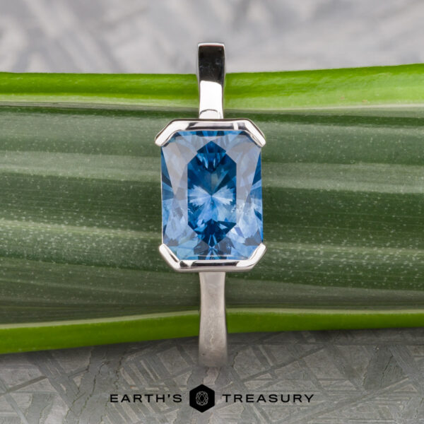 The "Lina" ring in 14k white gold with 2.34-Carat Montana Sapphire The "Lina" ring in 14k white gold with a 2.34-carat Montana sapphire is shown on a green striped leaf, with "Earth's Treasury" text at the bottom.