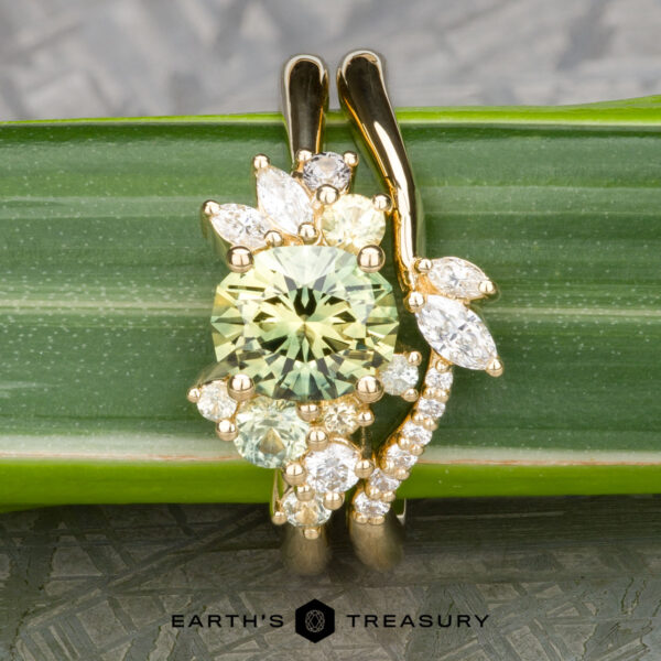 The "Liana" ring in 18k yellow gold with 1.50-carat Australian sapphire The "Liana" ring in 18k yellow gold features a 1.50-carat Australian sapphire and diamond accents, elegantly displayed on a green leaf with the Earth's Treasury logo at the bottom.