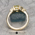 The "Liana" ring in 18k yellow gold with a 1.50-carat Australian sapphire stands upright on a rough blue stone, set against a geometric patterned background with "EARTH'S TREASURY" at the bottom.