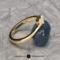 The "Liana" band in 18k yellow gold, featuring a clear gemstone, is displayed against a rugged dark mineral on a textured gray surface, with the Earth's Treasury logo below.