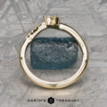 The "Liana" band in 18k yellow gold stands upright, encircling a rough blue stone at the center, set against a textured metallic background with "EARTH'S TREASURY" beneath.