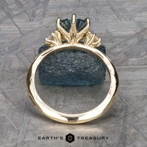 The "Clary" ring in 14k yellow gold, featuring a 1.43-carat Montana Sapphire in a prong setting, is displayed upright against a rough textured blue stone background.