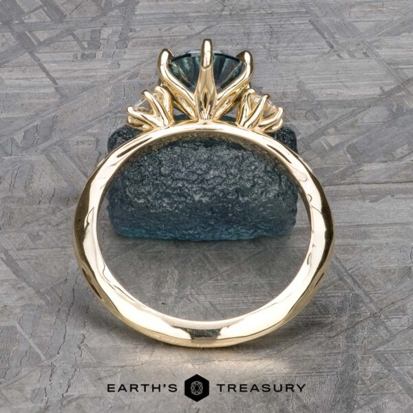 The "Clary" ring in 14k yellow gold with 1.43-Carat Montana Sapphire The "Clary" ring in 14k yellow gold, featuring a 1.43-carat Montana Sapphire in a prong setting, is displayed upright against a rough textured blue stone background.