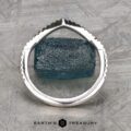 The "Graciella" band in 14k white gold stands upright with a jagged, textured edge framing a rough blue stone on a patterned gray surface featuring the Earth's Treasury logo.