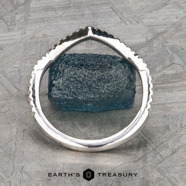The "Graciella" band in 14k white gold The "Graciella" band in 14k white gold stands upright with a jagged, textured edge framing a rough blue stone on a patterned gray surface featuring the Earth's Treasury logo.