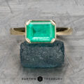 The "Marcy" Ring in 14k yellow gold features a 1.80-carat emerald-cut green gemstone resting on a rough stone surface, with "Earth's Treasury" below.