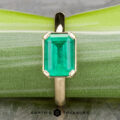 The "Marcy" Ring in 14k yellow gold showcases a 1.80-carat emerald in an upright, rectangular cut, displayed against a light green background.