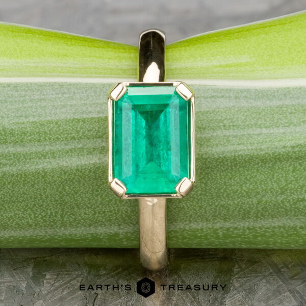 The "Marcy" Ring in 14k yellow gold with 1.80-Carat Emerald The "Marcy" Ring in 14k yellow gold showcases a 1.80-carat emerald in an upright, rectangular cut, displayed against a light green background.