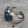 The "Lobelia" ring in platinum, featuring a 1.19-carat Montana sapphire, is displayed on a textured gray surface with the Earth’s Treasury logo at the bottom.