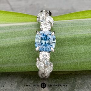 The "Lobelia" ring in platinum features a 1.19-carat Montana sapphire at its center, accented by white marquise and pear-shaped stones, beautifully displayed on a green leaf.