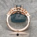 The "Celeste" ring in 14k rose gold with a 2.37-carat Montana sapphire is displayed upright on a textured gray surface, with the Earth's Treasury logo at the bottom.