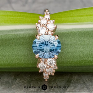 The "Celeste" ring in 14k rose gold showcases a 2.37-carat Montana sapphire with white accent stones, beautifully presented on a green leaf.