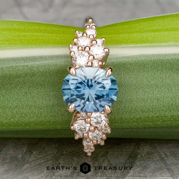 The "Celeste" ring in 14k rose gold showcases a 2.37-carat Montana sapphire with white accent stones, beautifully presented on a green leaf.