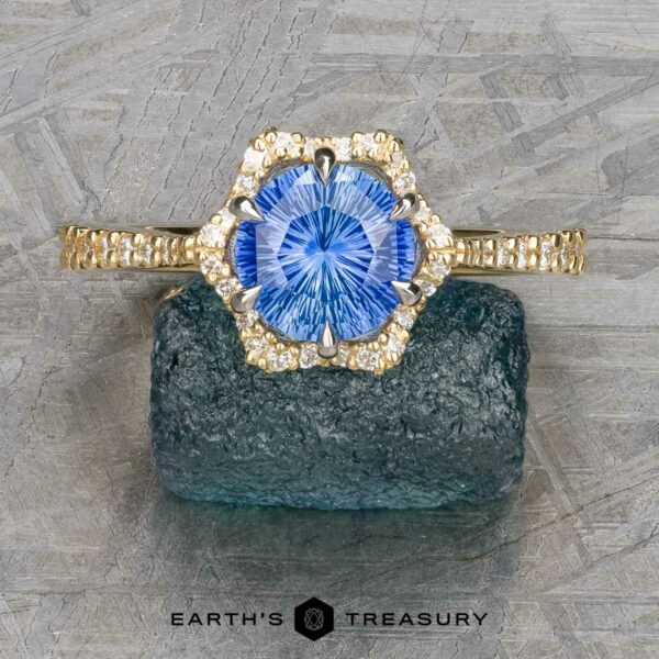 The "Plumeria" ring in 18k yellow and platinum with 1.18-carat Ceylon sapphire The "Plumeria" ring in 18k yellow and platinum features a 1.18-carat Ceylon sapphire surrounded by diamonds, displayed on dark stone with the "EARTH'S TREASURY" logo below.