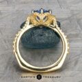 The "Plumeria" ring in 18k yellow and platinum, featuring a 1.18-carat Ceylon sapphire in an ornate prong setting, displayed upright on dark stone with “EARTH'S TREASURY” below.