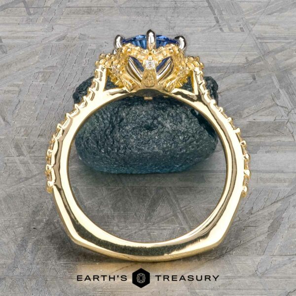 The "Plumeria" ring in 18k yellow and platinum with 1.18-carat Ceylon sapphire The "Plumeria" ring in 18k yellow and platinum, featuring a 1.18-carat Ceylon sapphire in an ornate prong setting, displayed upright on dark stone with “EARTH'S TREASURY” below.