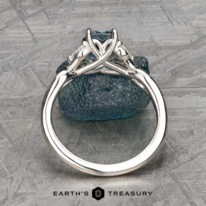 The "Anise" ring in platinum features a 1.37-carat Montana Sapphire in an intricate setting, displayed upright on a rough blue stone with the Earth's Treasury logo below.
