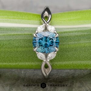 A platinum "Anise" ring featuring a 1.37-carat Montana Sapphire, marquise and round diamonds, displayed on a green striped background with the "Earth's Treasury" logo below.