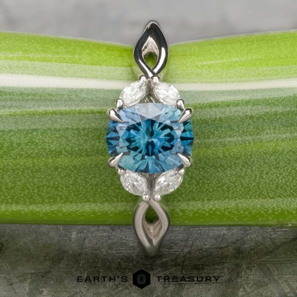 The "Anise" ring in platinum with 1.37-Carat Montana Sapphire A platinum "Anise" ring featuring a 1.37-carat Montana Sapphire, marquise and round diamonds, displayed on a green striped background with the "Earth's Treasury" logo below.