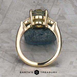 The "Dryad" ring in 14k yellow gold with a 3.50-carat Montana sapphire is displayed upright on a stone, with the Earth's Treasury logo at the bottom.