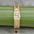 The "Augusta" ring features a 14k yellow gold band set with a 1.01-carat diamond, accented by baguette diamonds and displayed on a green stem with the Earth’s Treasury logo below.