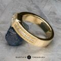 The "Augusta" ring in 14k yellow gold, set with a 1.01-carat diamond, rests against a dark uncut stone on a textured gray surface; the "Earth's Treasury" logo appears below.