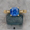 The "Marilyn" ring in 18k yellow gold, featuring a 3.20-carat Ceylon sapphire and diamond accents, is displayed on a rough dark stone with the Earth's Treasury logo below.