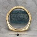 The "Marilyn" band in 18k yellow gold stands upright, encircling a rough blue stone on a textured grey background, with "Earth's Treasury" written below.